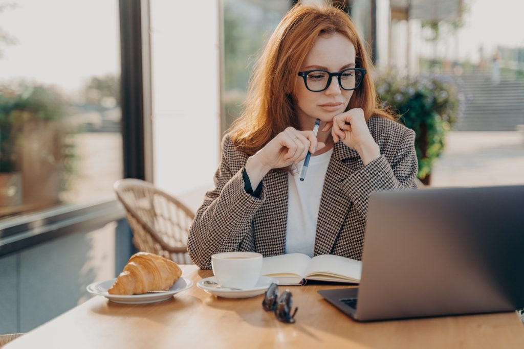 Serious ginger businesswoman in formal wear works in cafeteria develops new startup project